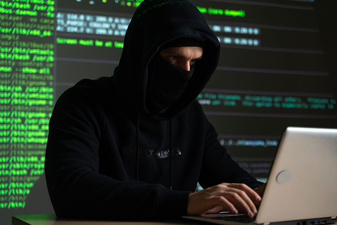 Hacker sitzt vor Laptop im Hintergrund grüne Codezeilen